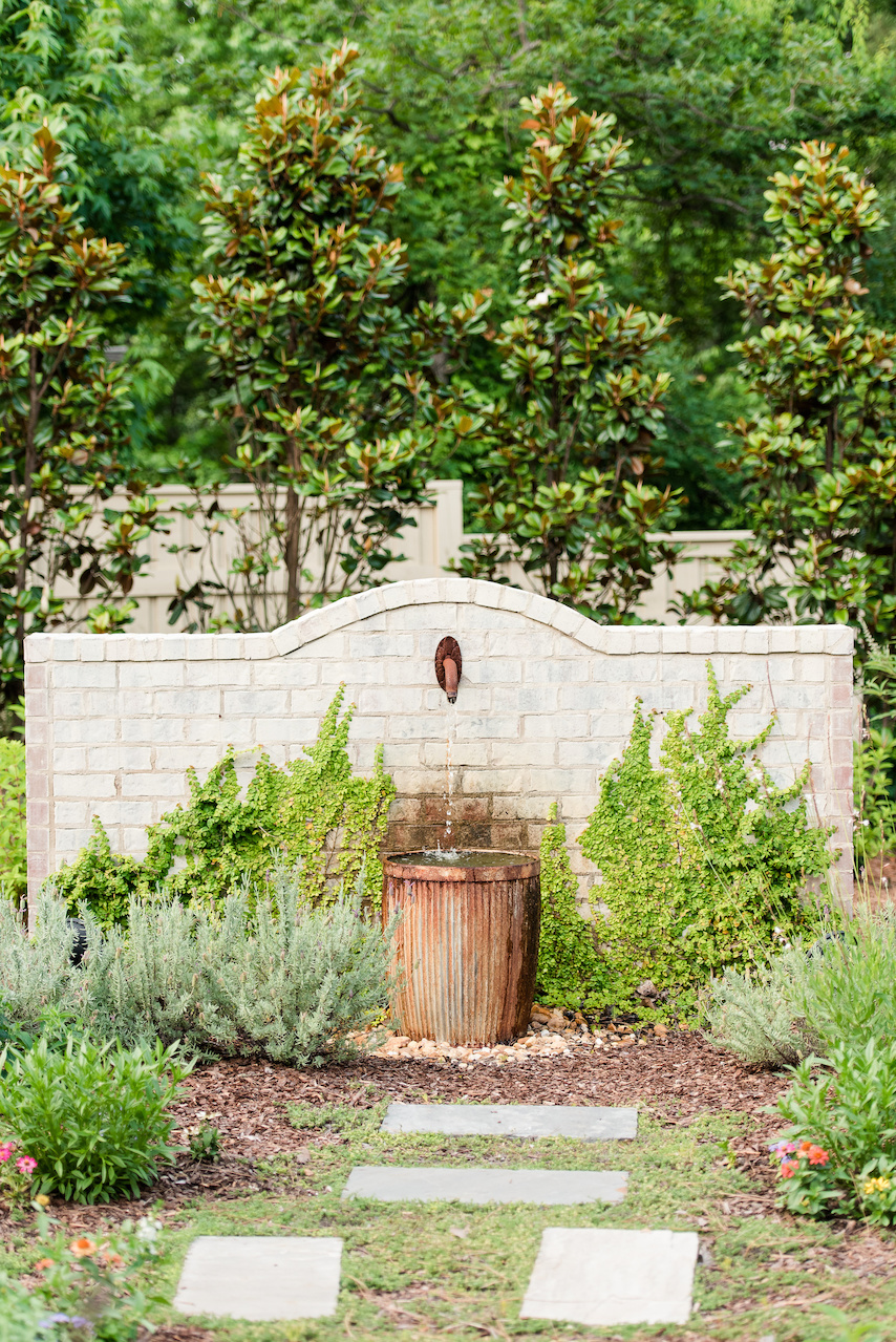 The freestanding fountain wall features an antique spigot from Architectural Heritage and a metal corrugated plant bucket, set on a basin of pea gravel. "It really ties the whole garden together," says Clarke. The freestanding fountain wall features an antique spigot from Architectural Heritage and a metal corrugated plant bucket, set on a basin of pea gravel. "It really ties the whole garden together," says Clarke.