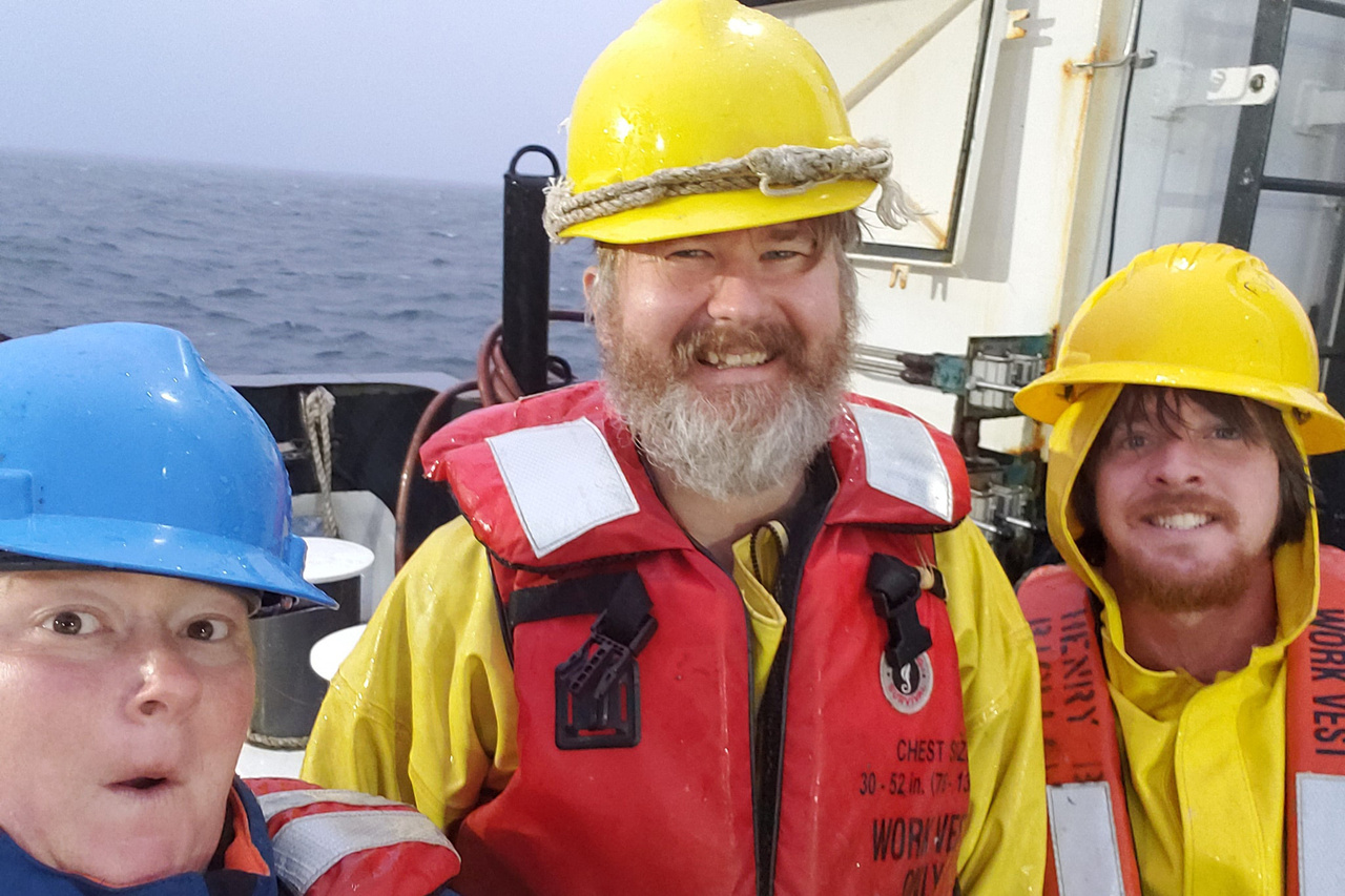 three scientists in life jackets and hard hats on the deck of a research vessel