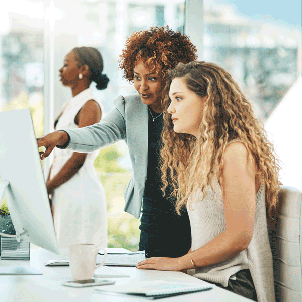 woman in suit showing woman with long hair something on a silver display screen
