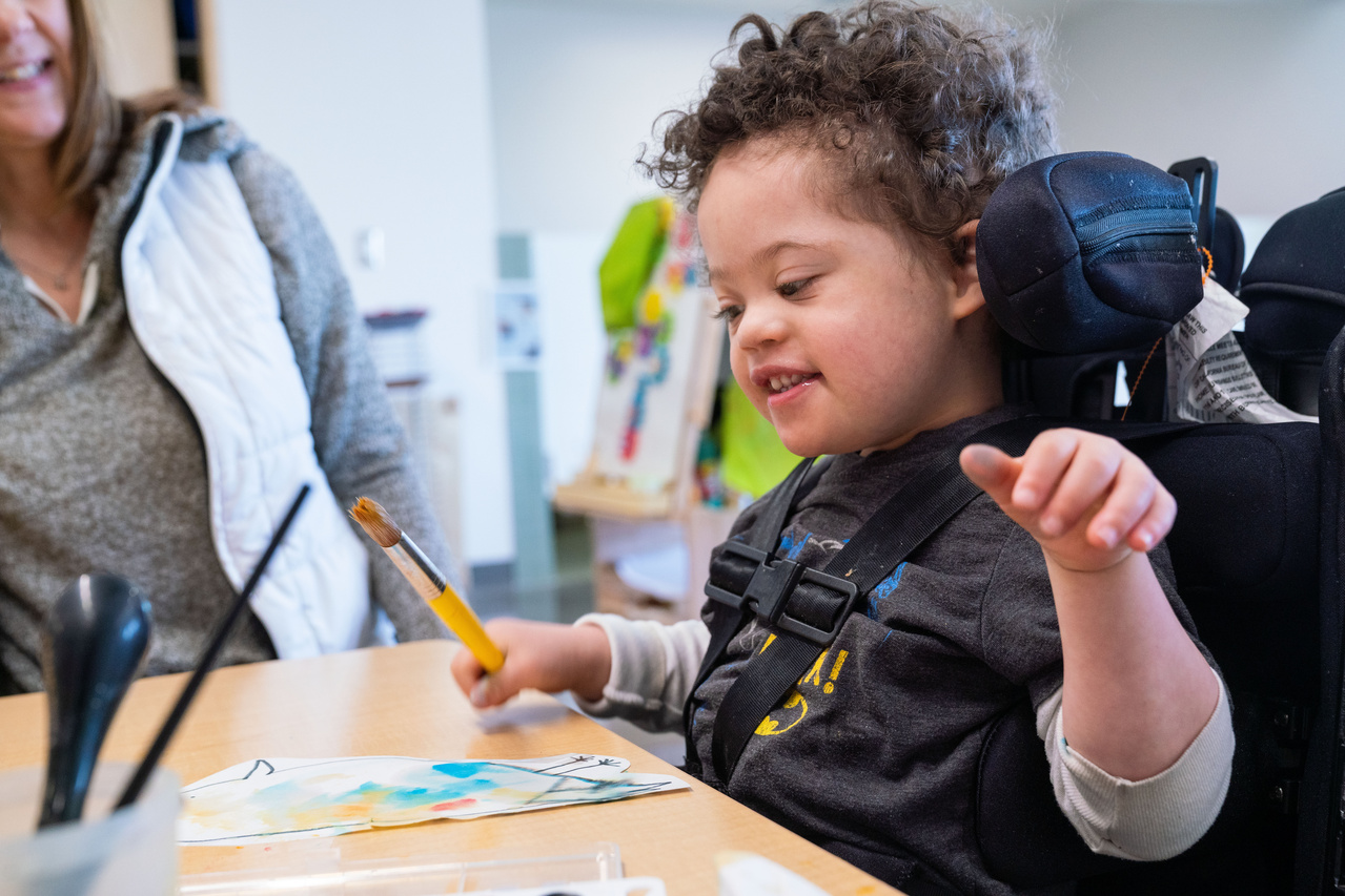 A child smiles while painting in an accessible seat.