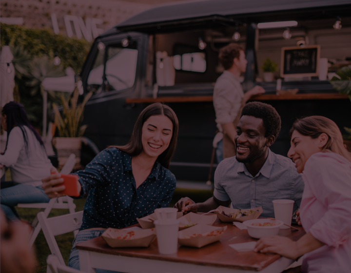 Group of three taking selfie at picnic table eating food at outdoor food truck