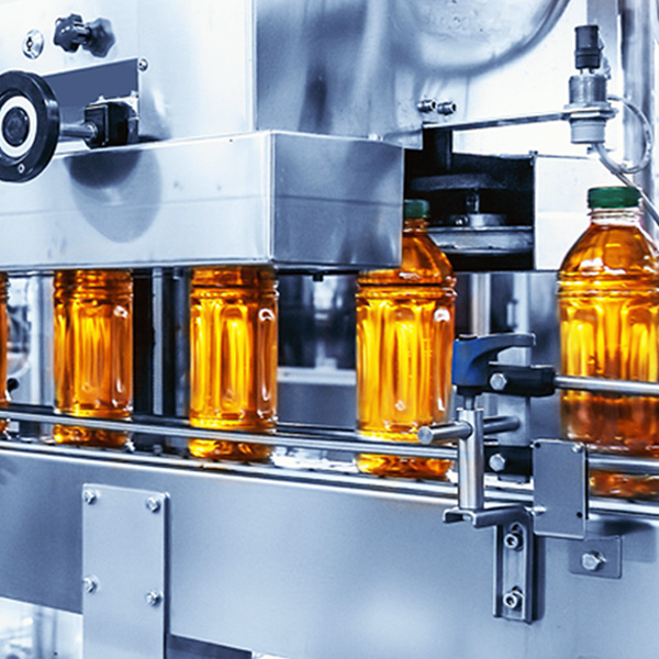 Clear plastic bottles with green caps and filled with apple juice move along a silver-colored bottling line