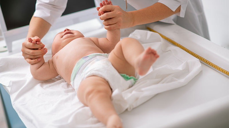 Baby laying on small bed while doctor holds its hands up