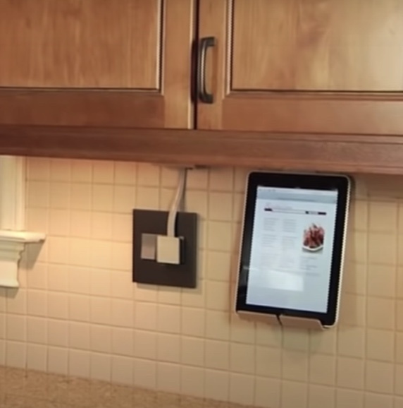 under cabinet lighting plugged in in brown and white kitchen with tablet on cradle with recipe