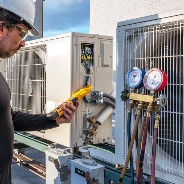 A technician uses a yellow handheld device while checking gauges for a HVAC system