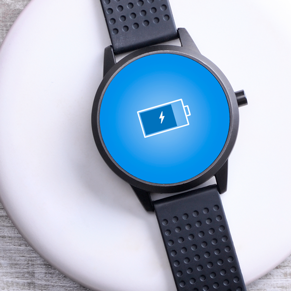 A round-faced smartwatch with a black band charges on a white wireless charging pad
