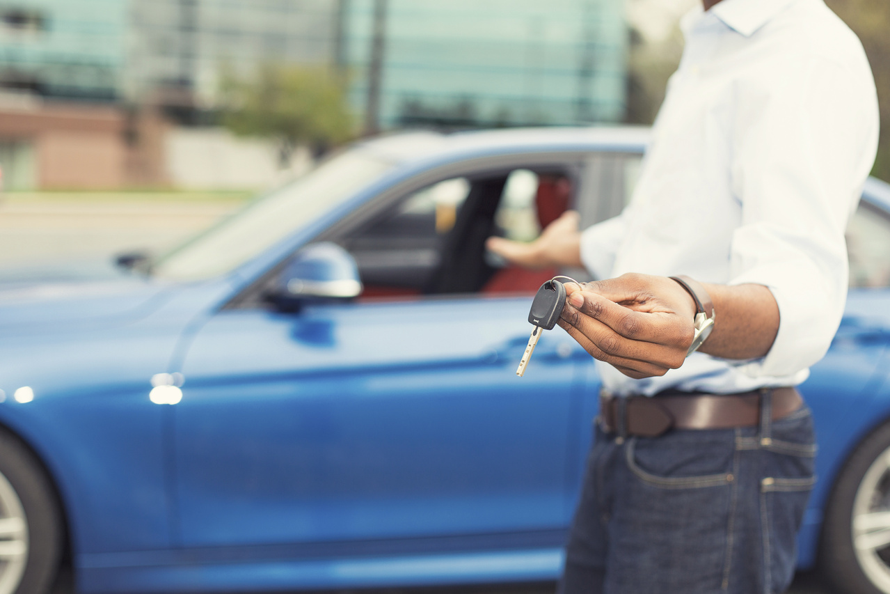 Man handing car key towards camera, blurred car in background