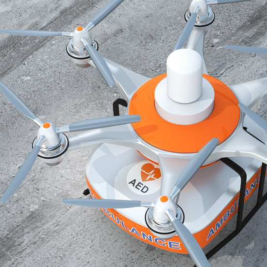 Closeup of a quad copter with an orange and white automated external defibrillator (AED) marked "AMBULANCE" attached
