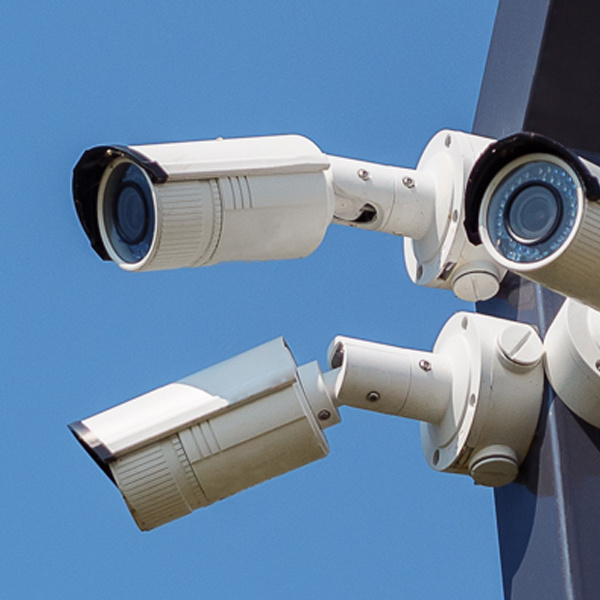 Four security cameras attached to a light pole in a parking lot point in all directions