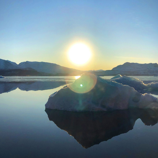 Water smooth as glass as the sun rises over mountains lining the Qaqortoq fjord in southwest Greenland.
